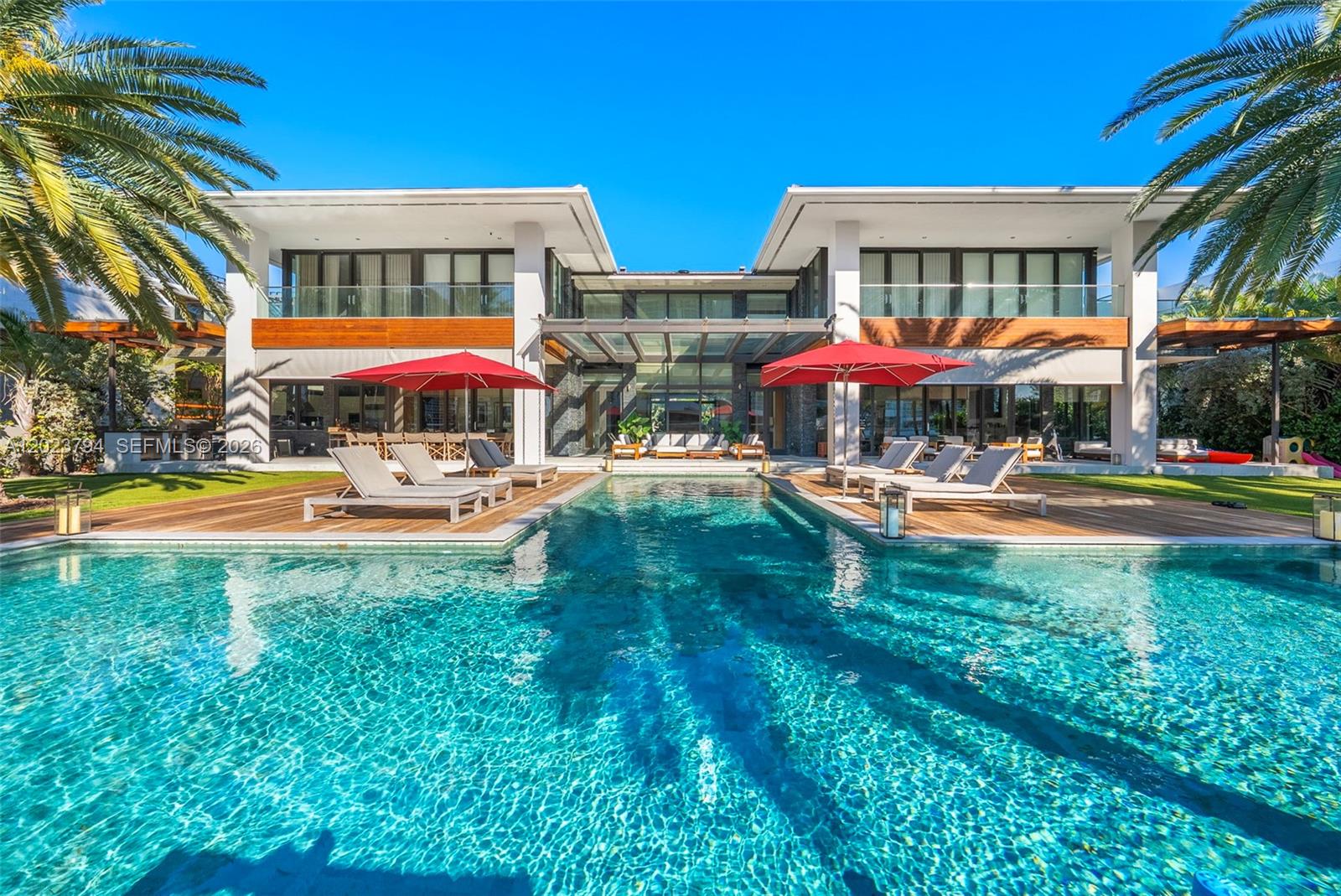 A modern two-story house features a swimming pool, wooden decking, and red patio umbrellas — 385 Centre Is, Golden Beach FL 33160, GOLDEN BEACH, FL