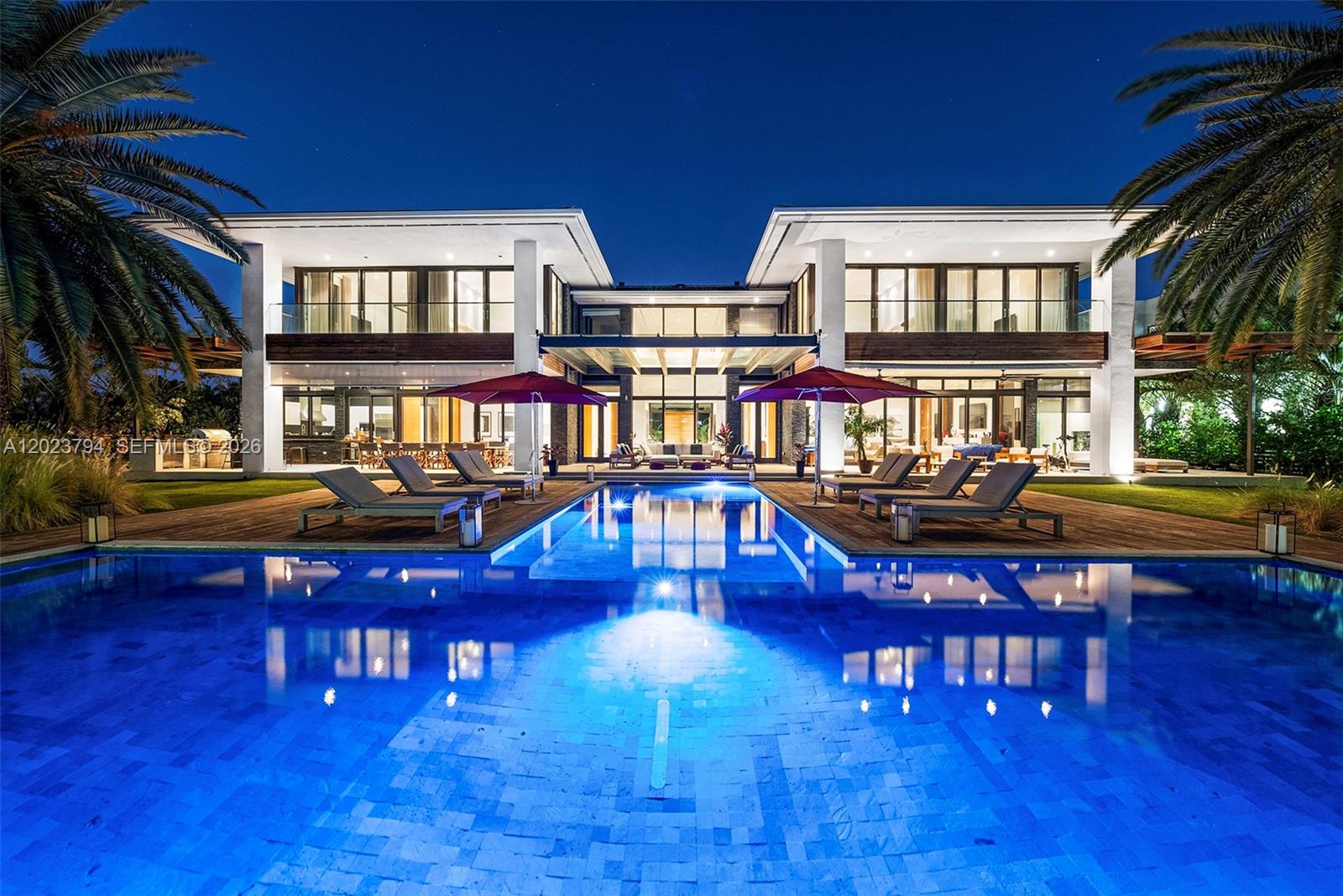 A modern two-story luxury home features a large swimming pool and patio at night — 385 Centre Is, Golden Beach FL 33160, GOLDEN BEACH, FL