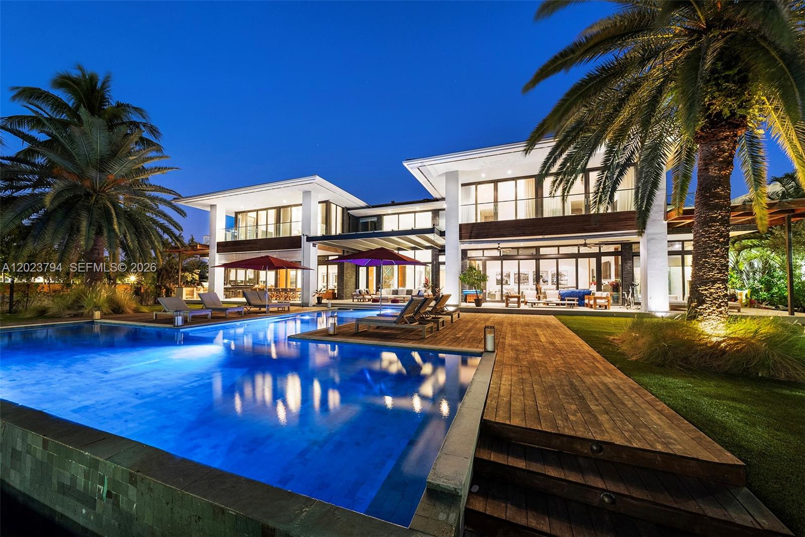A modern two-story house features a swimming pool, wooden deck, and palm trees at night — 385 Centre Is, Golden Beach FL 33160, GOLDEN BEACH, FL