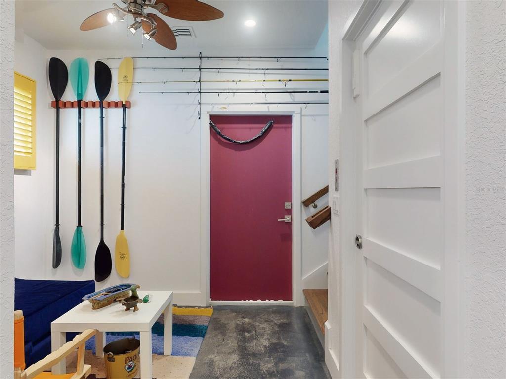 A room with a red door, wall-mounted paddles, fishing rods, and a white coffee table — 901 SHEEPSHEAD AVENUE, NEW SMYRNA BEACH, FL