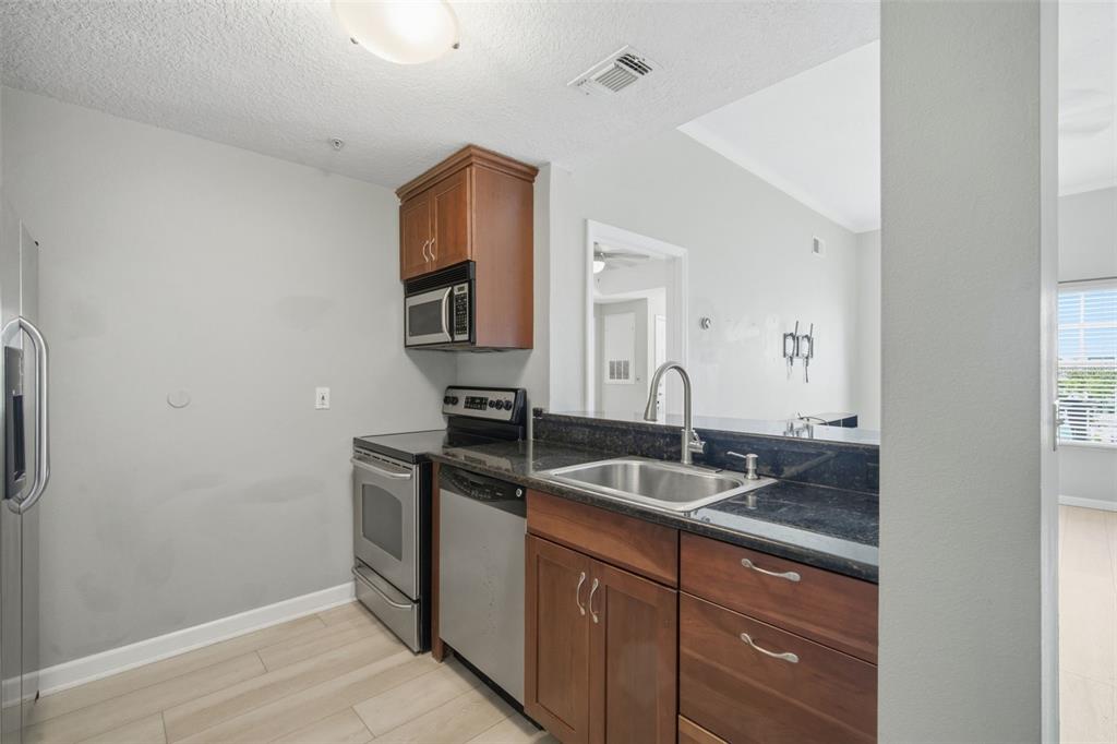A kitchen features wood cabinets, dark granite countertops, stainless steel appliances, and light flooring — 800 S DAKOTA AVENUE UNIT 435, TAMPA, FL