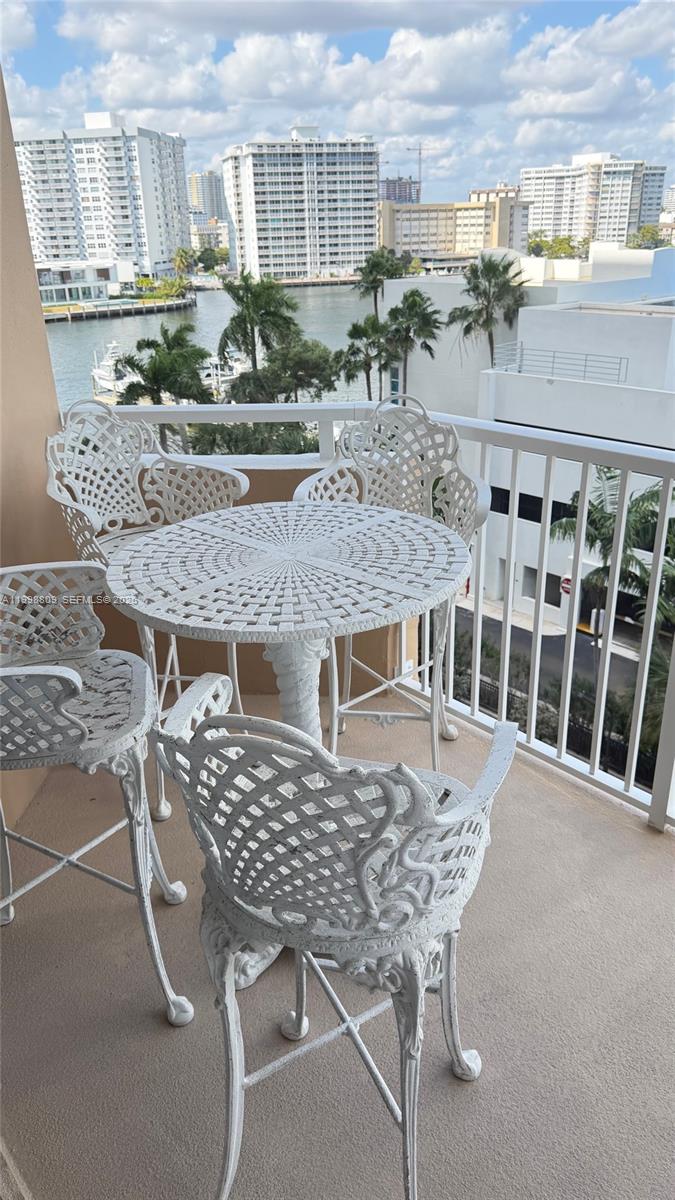 A balcony features a white metal table and four matching chairs overlooking a waterfront cityscape — 1965 S Ocean Dr # 5D, Hallandale Beach FL 33009, HALLANDALE BEACH, FL