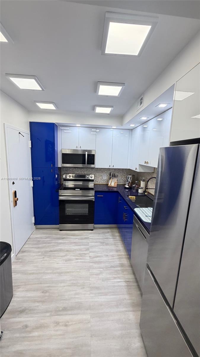 A modern kitchen features blue and white cabinetry, stainless steel appliances, and light wood flooring — 1965 S Ocean Dr # 5D, Hallandale Beach FL 33009, HALLANDALE BEACH, FL