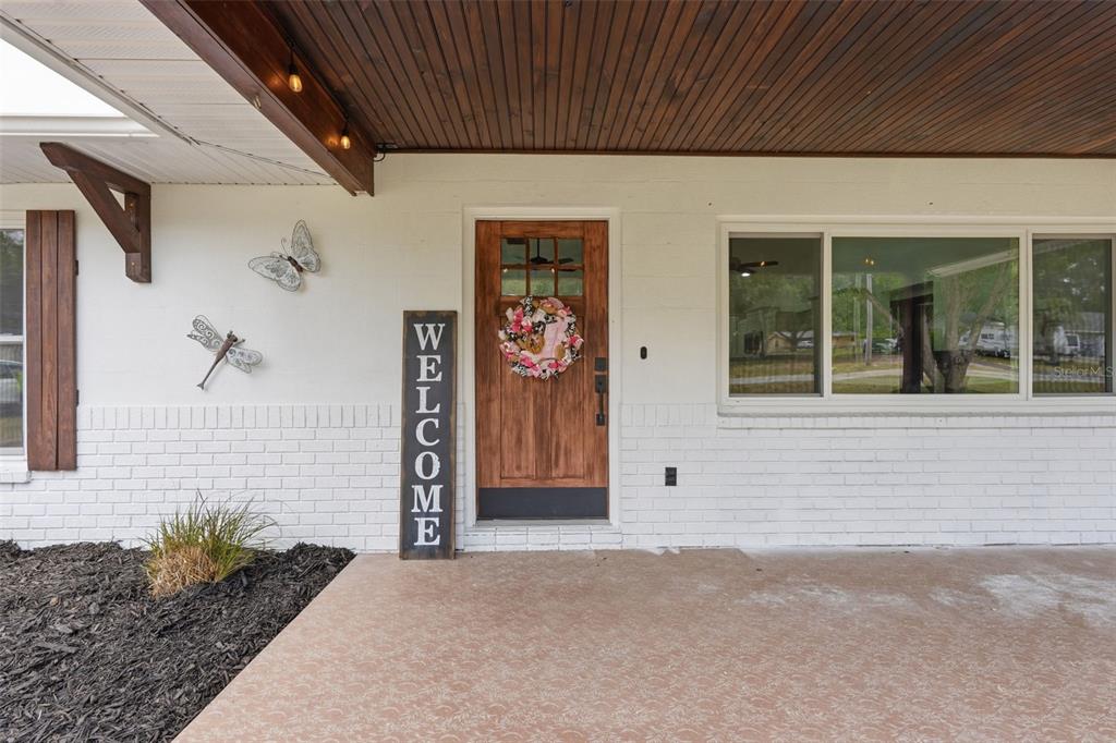 A white brick house exterior features a wood front door, a welcome sign, and decorations — 39825 SUNBURST DRIVE, DADE CITY, FL
