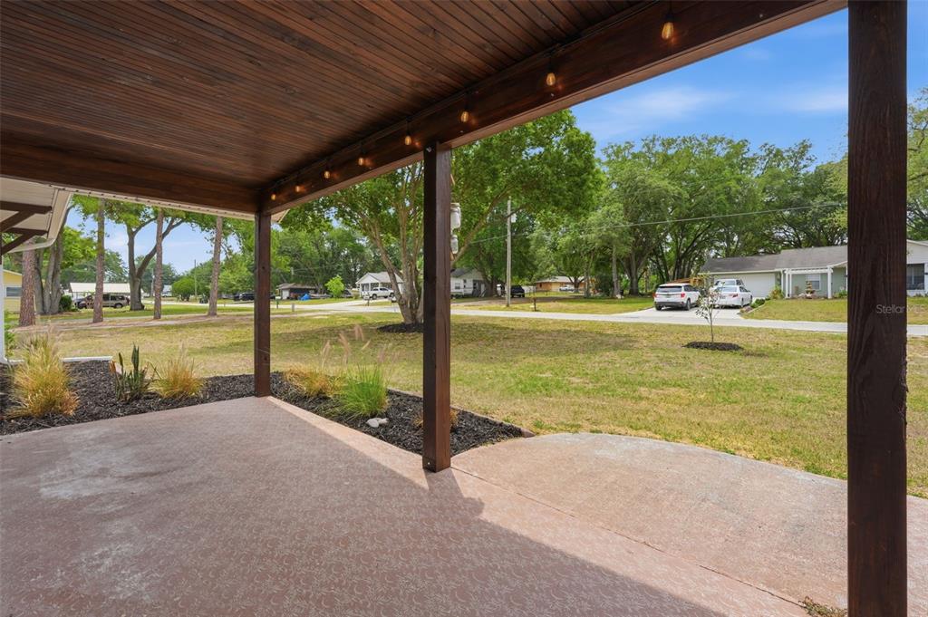 A covered patio with a wood-paneled ceiling overlooks a grassy residential yard and street — 39825 SUNBURST DRIVE, DADE CITY, FL