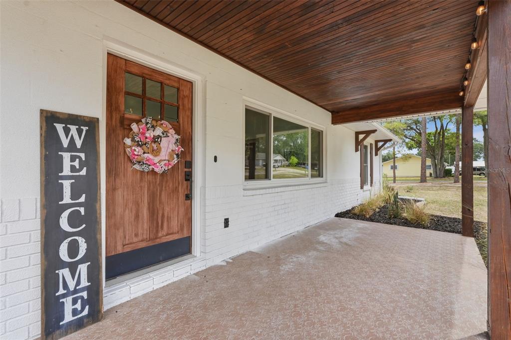 A covered front porch with a white brick wall, wooden ceiling, and a wooden door — 39825 SUNBURST DRIVE, DADE CITY, FL