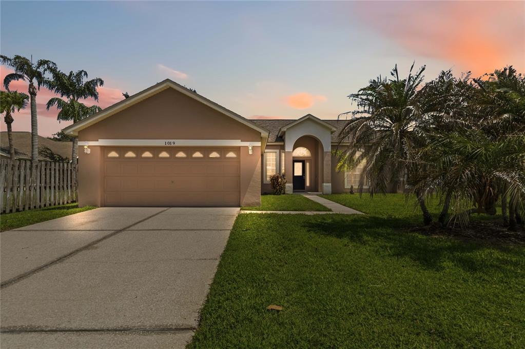 A single-story house with a tan stucco exterior, a two-car garage, and a palm tree — 1019 CHAMBERLIN TRAIL, ST CLOUD, FL