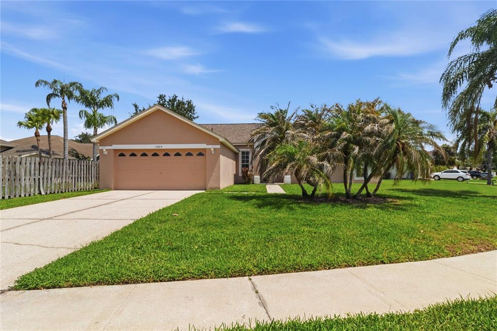 A single-story house with a tan exterior, a two-car garage, and palm trees in front — 1019 CHAMBERLIN TRAIL, ST CLOUD, FL
