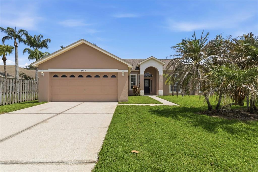 A tan single-story house with a two-car garage, arched entryway, and palm trees — 1019 CHAMBERLIN TRAIL, ST CLOUD, FL