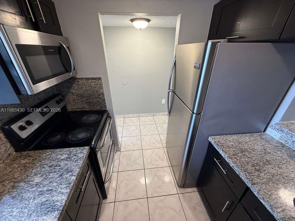 A kitchen features dark cabinets, granite countertops, stainless steel appliances, and light tile flooring — 2721 NW 23rd Ct # 4, Miami FL 33142, MIAMI, FL