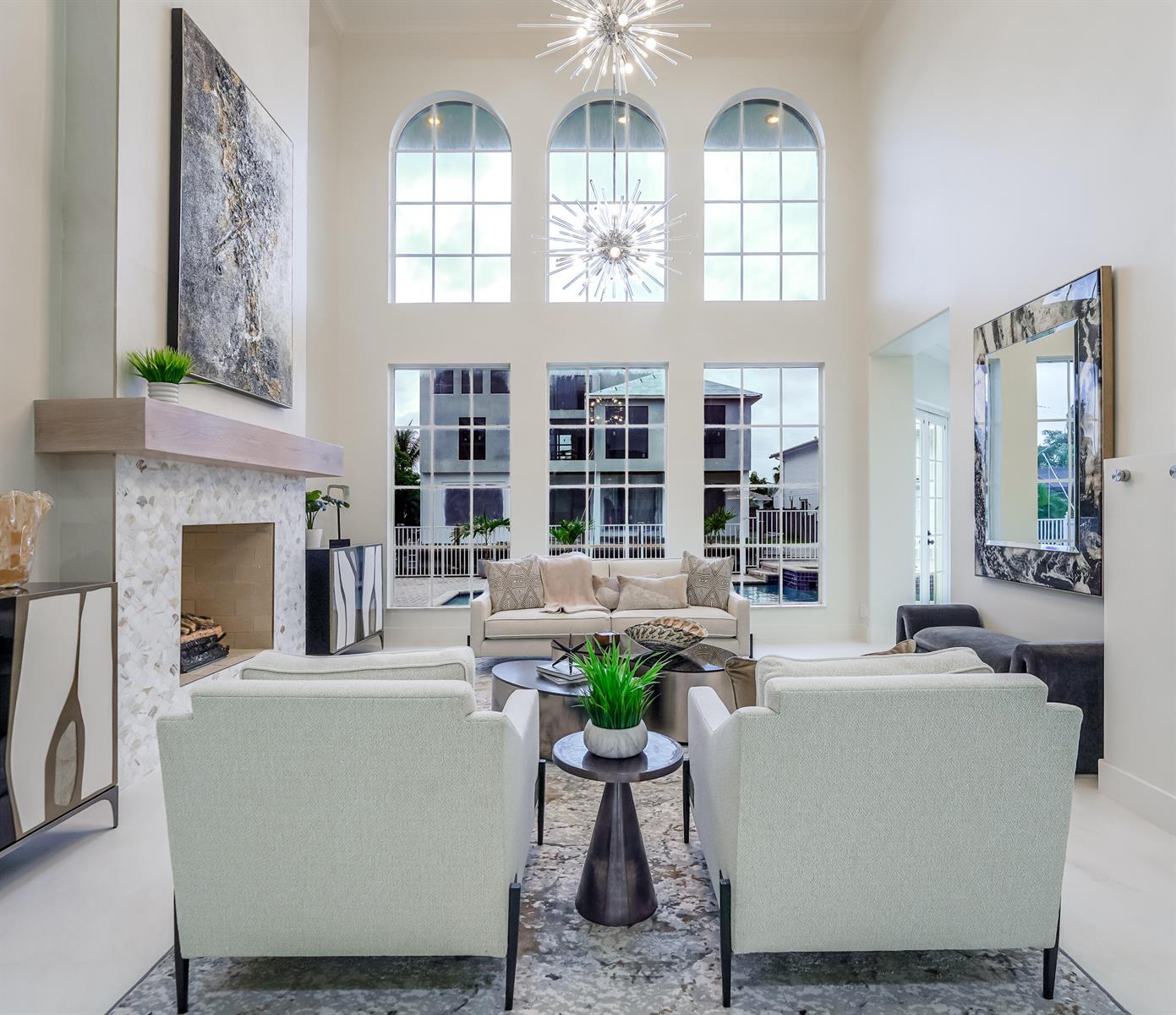 A bright living room features a fireplace, tall arched windows, and two modern chandeliers — 749 NE 71st Street, Boca Raton FL 33487, BOCA RATON, FL