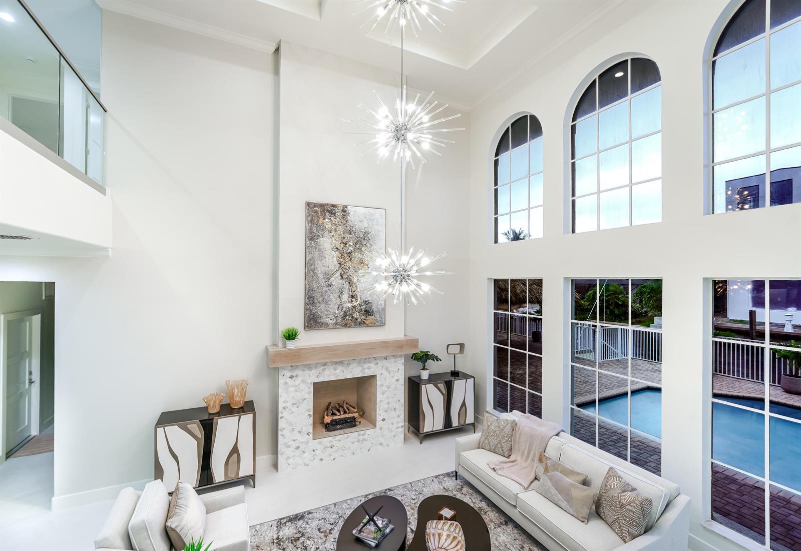 A high-ceilinged living room features a fireplace, two starburst chandeliers, and large arched windows — 749 NE 71st Street, Boca Raton FL 33487, BOCA RATON, FL