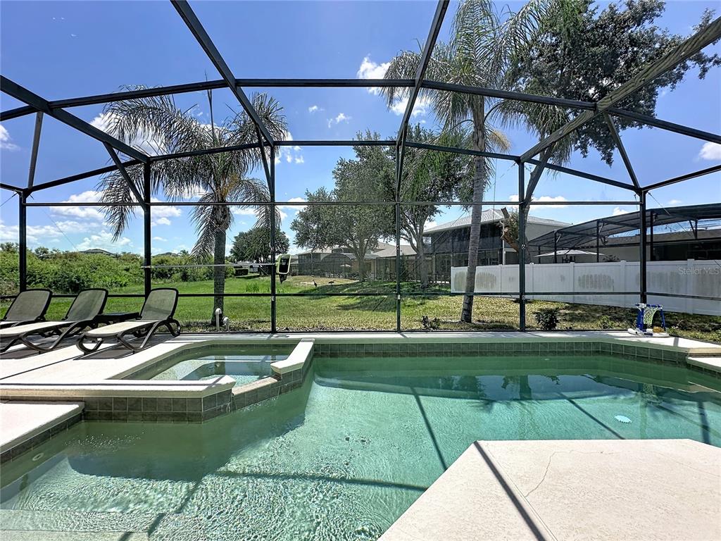 A screened-in pool and spa area with lounge chairs overlooking a grassy backyard — 906 DORSET PLACE, DAVENPORT, FL