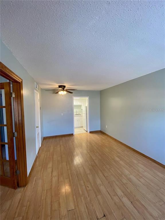 A room with light wood flooring, a ceiling fan, and a doorway leading to a kitchen — 551 FLEMMING WAY UNIT 201, MAITLAND, FL