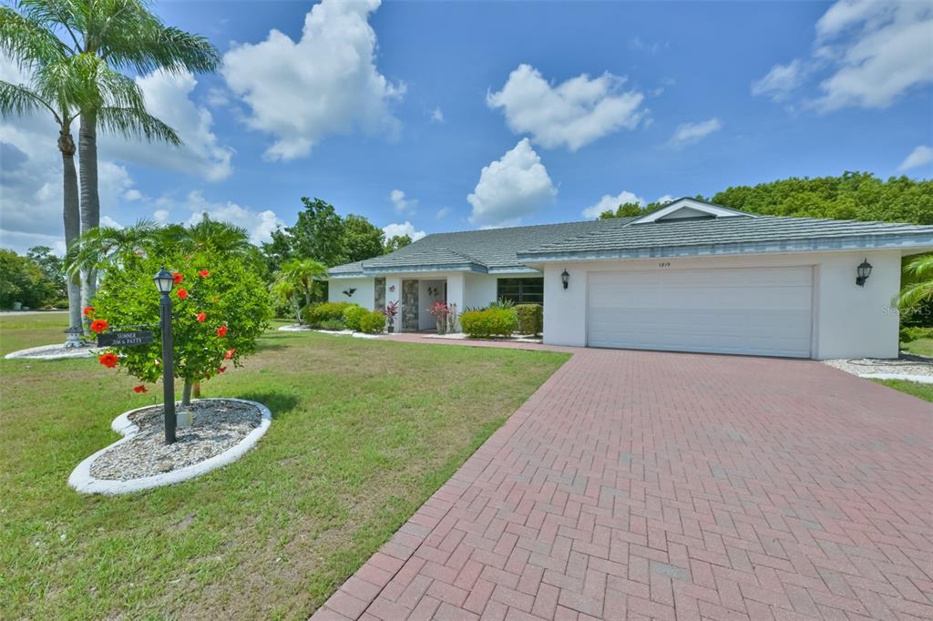 A single-story house with a white exterior, a brick driveway, and a palm tree — 1819 NEW BEDFORD DRIVE, SUN CITY CENTER, FL