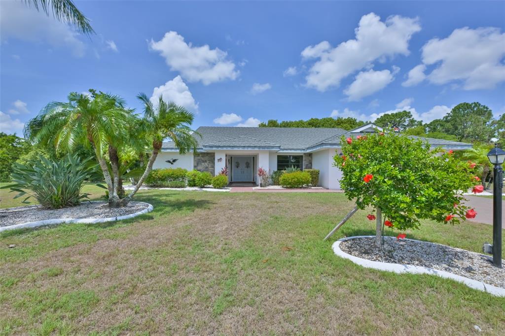 A single-story house with a light-colored exterior, stone accents, and a landscaped front yard — 1819 NEW BEDFORD DRIVE, SUN CITY CENTER, FL
