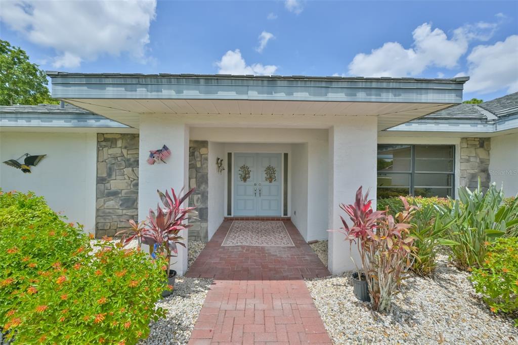 The exterior of a house features a brick walkway leading to light blue double front doors — 1819 NEW BEDFORD DRIVE, SUN CITY CENTER, FL
