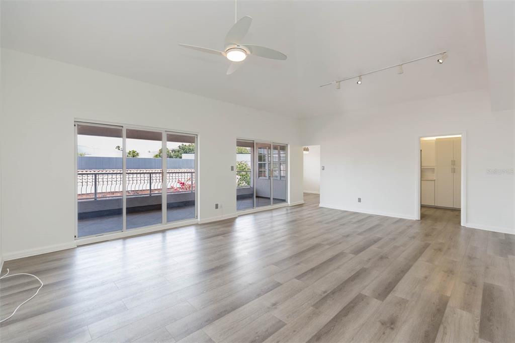 A spacious, white-walled living room features light wood-look flooring, a ceiling fan, and sliding glass doors — 1653 W SNOW CIRCLE UNIT 1653, TAMPA, FL