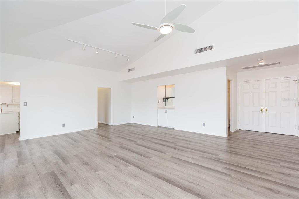 A spacious, white-walled living room features vaulted ceilings, a ceiling fan, and light wood flooring — 1653 W SNOW CIRCLE UNIT 1653, TAMPA, FL