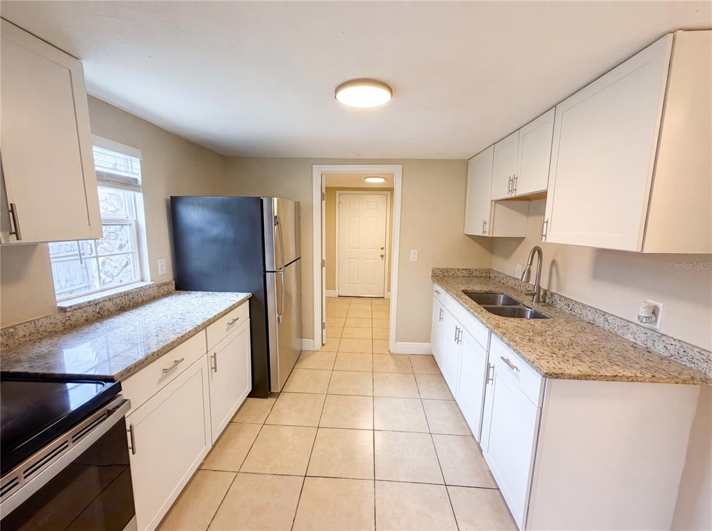 A kitchen features white cabinets, granite countertops, stainless steel appliances, and light tile flooring — 1506 W 16TH STREET, SANFORD, FL