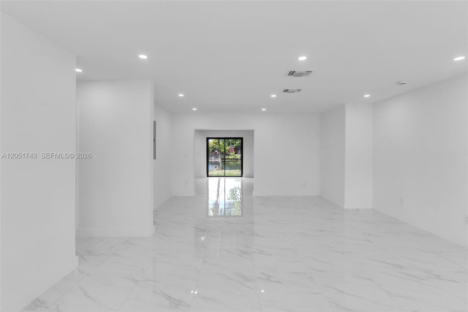 A bright, empty room features white marble-look tile flooring and a view of a lake — 12846 SW 49th Ter, Miami FL 33175, MIAMI, FL