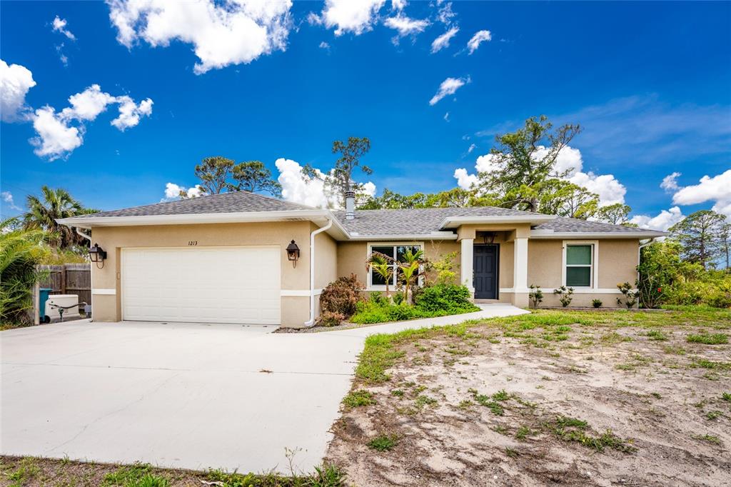 A single-story house with a beige stucco exterior, a two-car garage, and a concrete driveway — 1213 CASPER STREET, PORT CHARLOTTE, FL