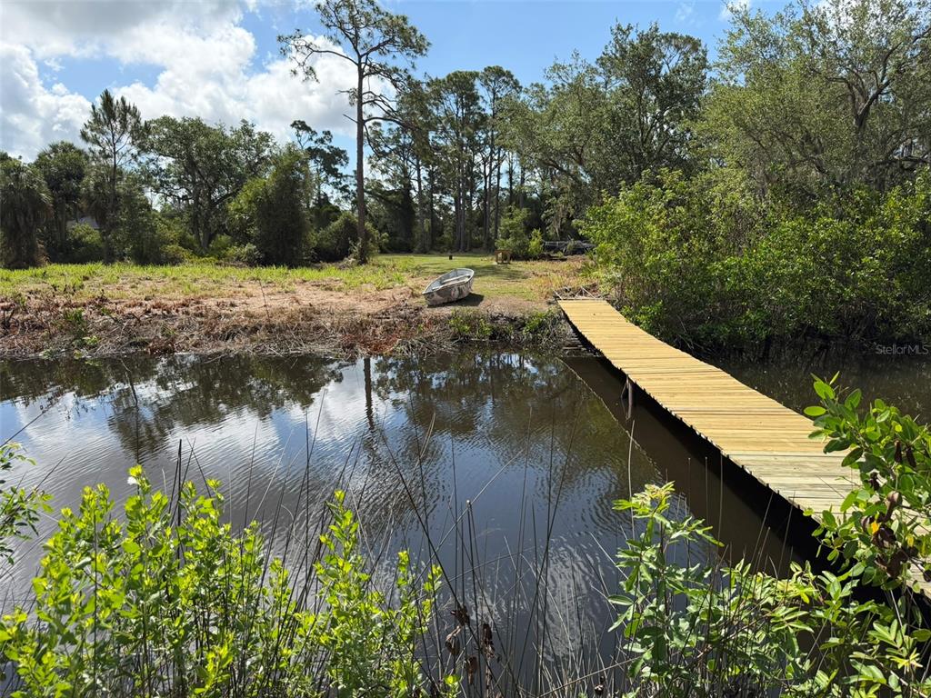 A wooden dock extends into a small pond near a grassy yard with a boat — 1213 CASPER STREET, PORT CHARLOTTE, FL