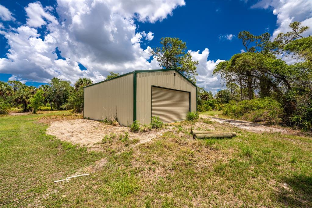 A detached metal storage shed sits on a sandy lot surrounded by trees and grass — 1213 CASPER STREET, PORT CHARLOTTE, FL