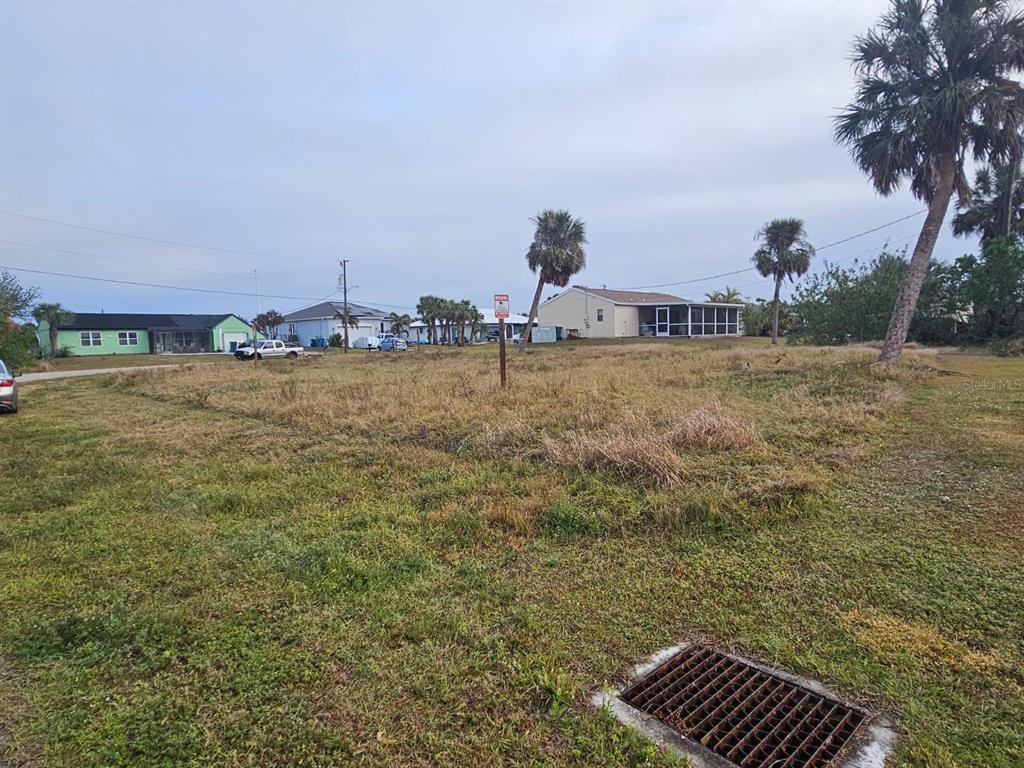 A vacant, grassy residential lot with a storm drain in the foreground and nearby houses — 18599 ASHCROFT CIRCLE, PORT CHARLOTTE, FL