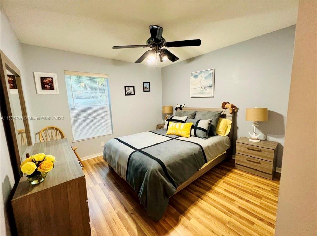 A bedroom features a bed with gray bedding, a wooden dresser, and a ceiling fan — 6972 NW 19th Street, Margate FL 33063, MARGATE, FL