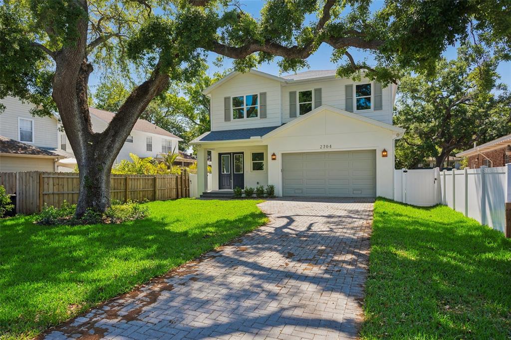 A two-story house with a paved driveway, a large tree, and a white fence — 2704 W TYSON AVENUE, TAMPA, FL