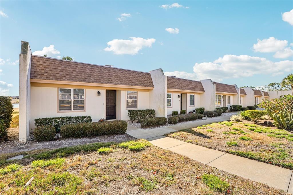 A row of single-story townhomes with beige siding, shingled roofs, and a concrete walkway — 11120 CARRIAGE HILL DRIVE UNIT 1, PORT RICHEY, FL