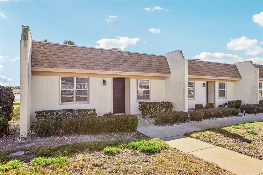 A row of single-story townhomes with beige siding, brown shingled roofs, and small front gardens — 11120 CARRIAGE HILL DRIVE UNIT 1, PORT RICHEY, FL