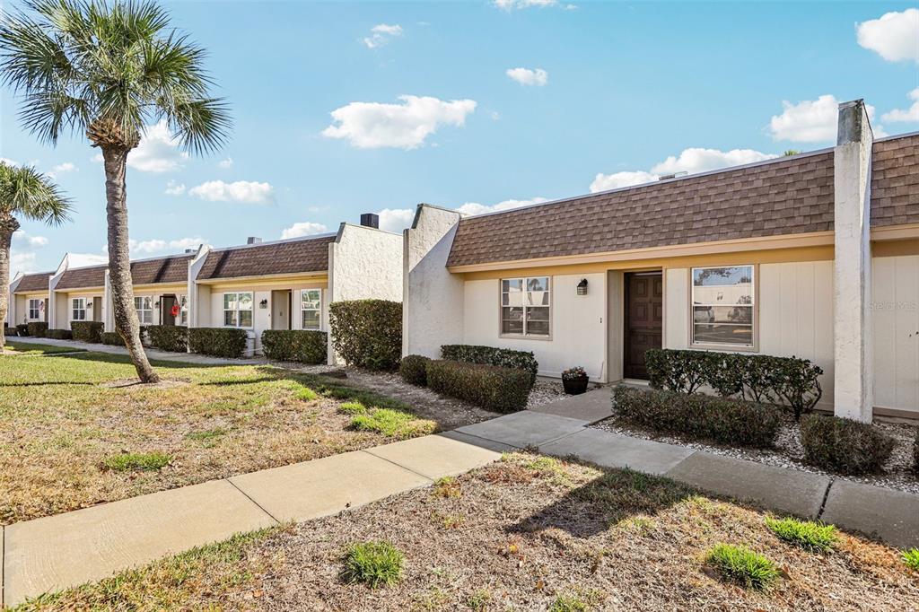 A row of single-story townhomes with beige siding, brown shingled roofs, and manicured landscaping — 11120 CARRIAGE HILL DRIVE UNIT 1, PORT RICHEY, FL