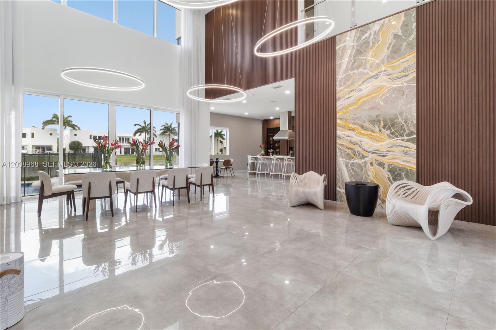 A modern, high-ceilinged dining room features a marble accent wall, circular pendant lights, and tile flooring — 10261 NW 74th Ter, Doral FL 33178, DORAL, FL