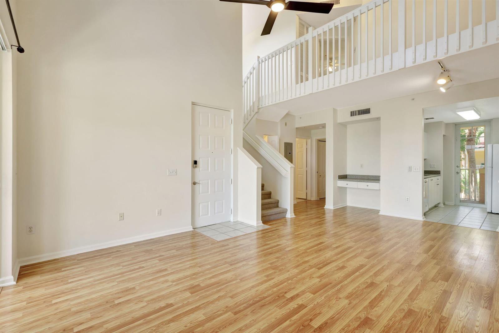 A living room with wood flooring, a staircase, a loft railing, and an entryway door — 4812 S Central Boulevard # 24, Jupiter FL 33458, JUPITER, FL