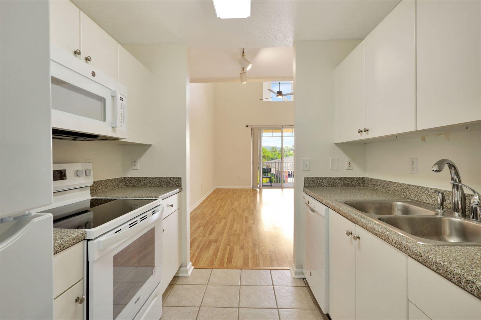 A galley kitchen with white cabinets and granite countertops opens to a living area beyond — 4812 S Central Boulevard # 24, Jupiter FL 33458, JUPITER, FL