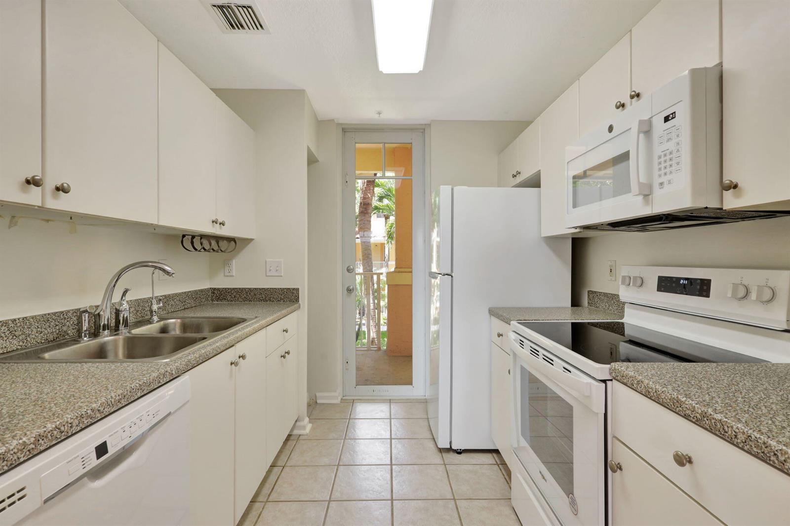 A galley kitchen features white cabinets, granite countertops, white appliances, and a glass door to a balcony — 4812 S Central Boulevard # 24, Jupiter FL 33458, JUPITER, FL