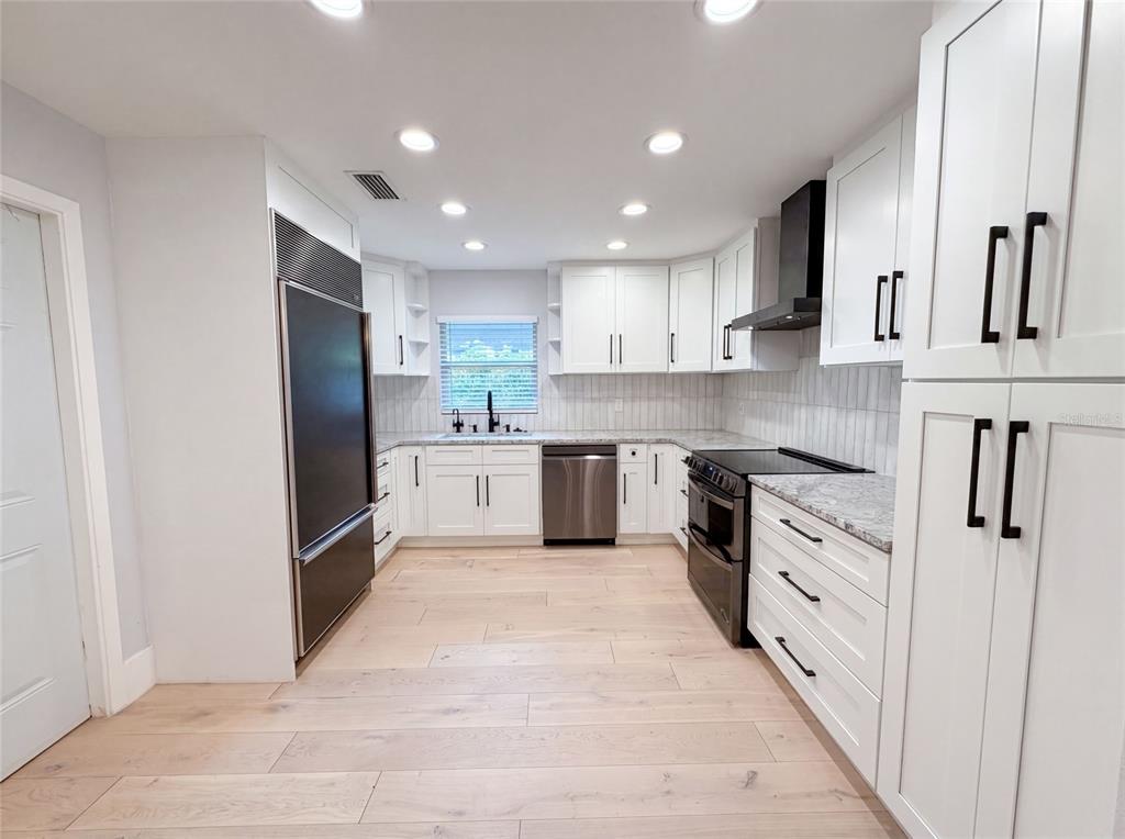 A modern kitchen features white cabinets, stainless steel appliances, and light wood-look flooring — 8028 CONSERVATORY CIRCLE, SARASOTA, FL