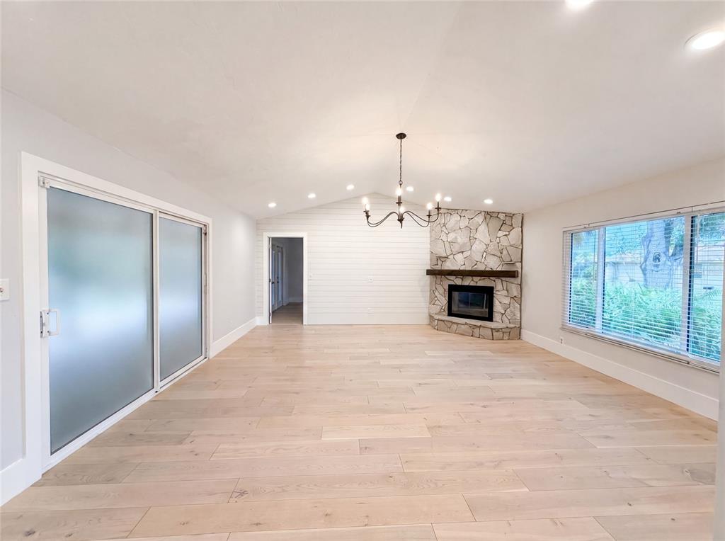 A bright living room features light wood flooring, a stone fireplace, and a vaulted ceiling — 8028 CONSERVATORY CIRCLE, SARASOTA, FL