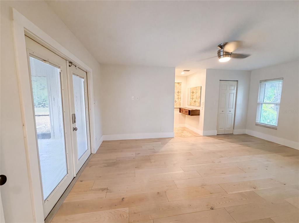 A bright room features light wood flooring, double glass doors, a ceiling fan, and a closet — 8028 CONSERVATORY CIRCLE, SARASOTA, FL