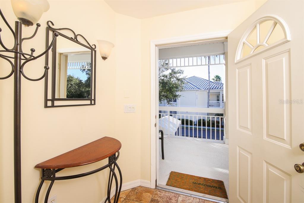An entryway features a console table, a wall mirror, and an open door to a balcony — 3605 54TH DRIVE W UNIT 202, BRADENTON, FL