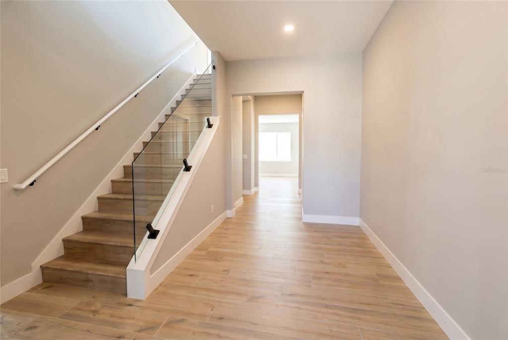 A modern entryway features wood-look tile flooring, a glass-railed staircase, and a view into another room — 16046 VETTA DRIVE, BELLA COLLINA, FL