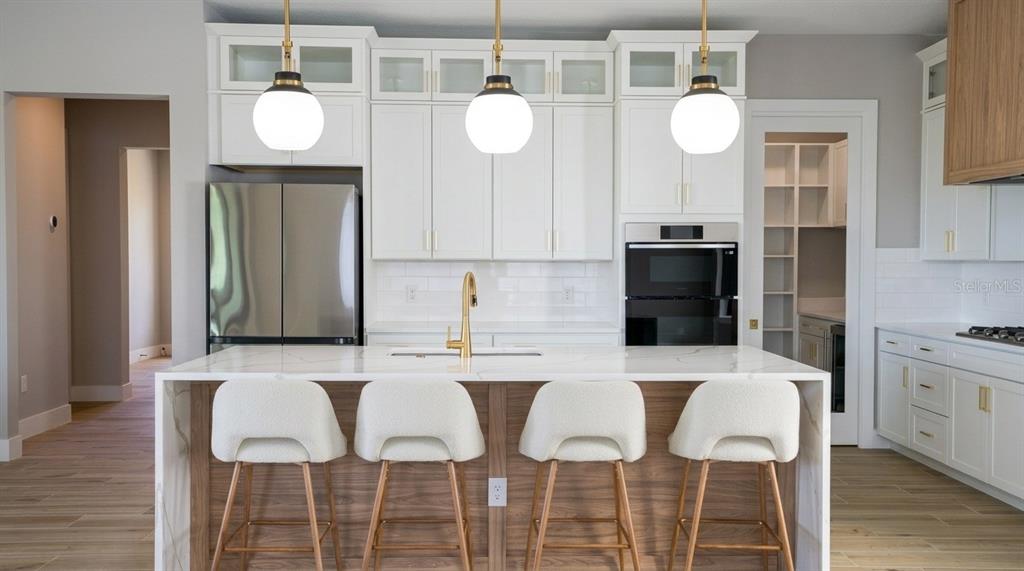 A modern kitchen features white cabinetry, a marble-topped island with four stools, and stainless appliances — 16046 VETTA DRIVE, BELLA COLLINA, FL
