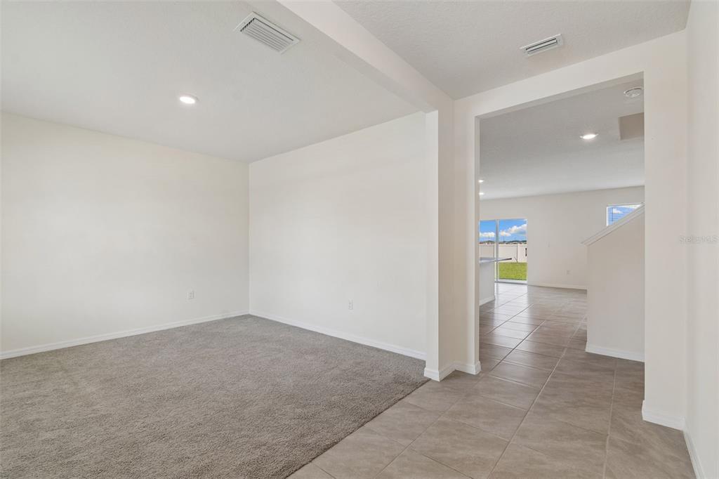 A carpeted room transitions into a tiled hallway leading toward a bright, open living area — 8454 ENDER HILLS DRIVE, WESLEY CHAPEL, FL