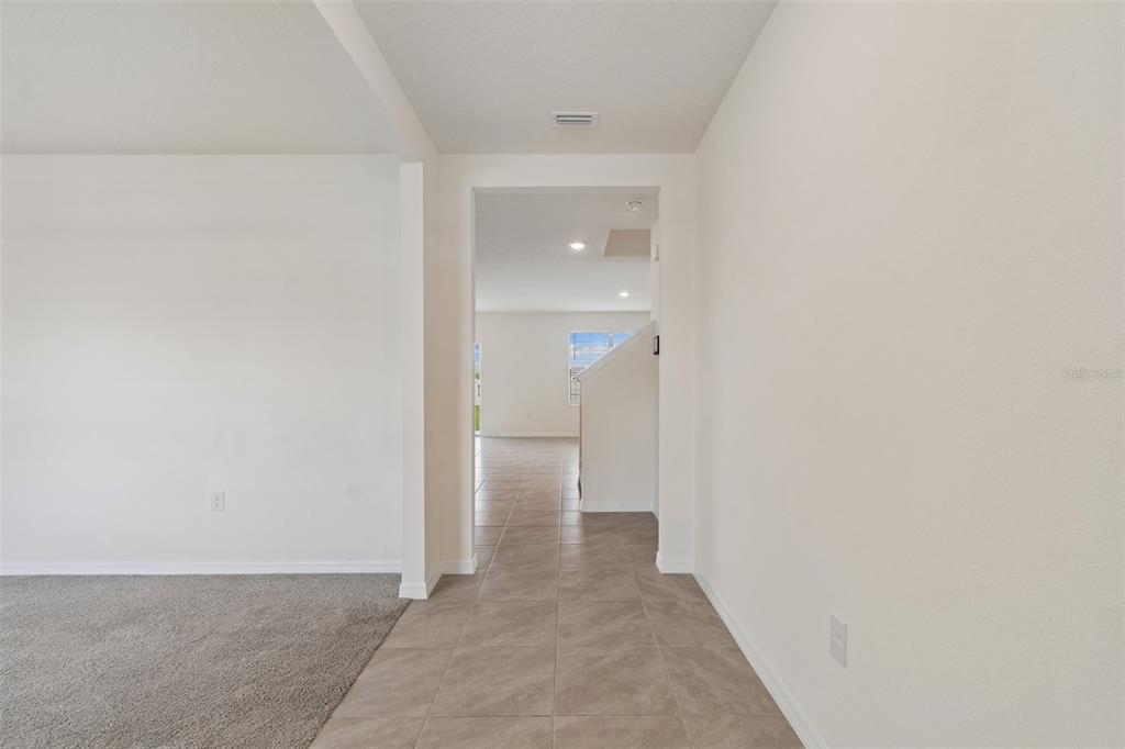 A view from a carpeted room through a tiled hallway toward a bright living area — 8454 ENDER HILLS DRIVE, WESLEY CHAPEL, FL