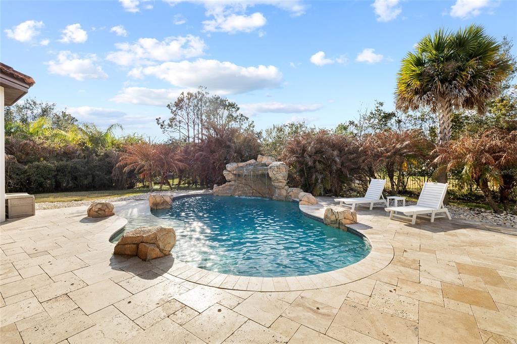 A backyard swimming pool features a rock waterfall, stone decking, and two white lounge chairs — 16406 CHAPMAN CROSSING DRIVE, LITHIA, FL