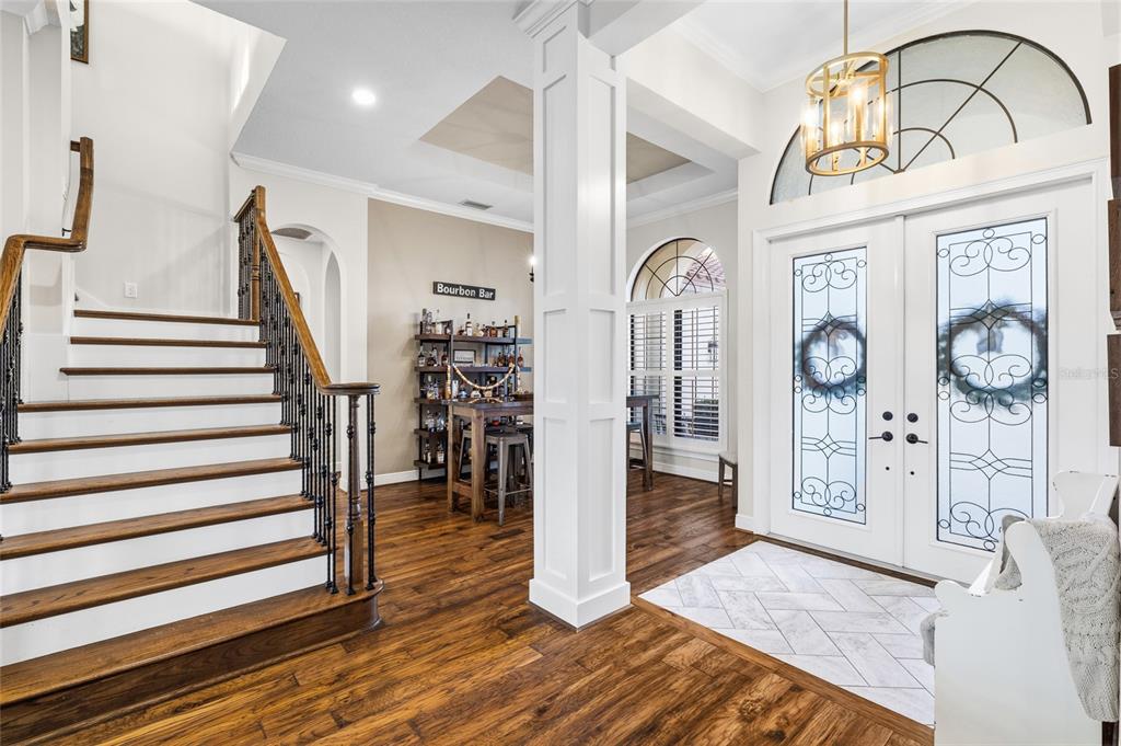 A foyer features a wooden staircase, a bourbon bar, and double front doors with glass inserts — 16406 CHAPMAN CROSSING DRIVE, LITHIA, FL