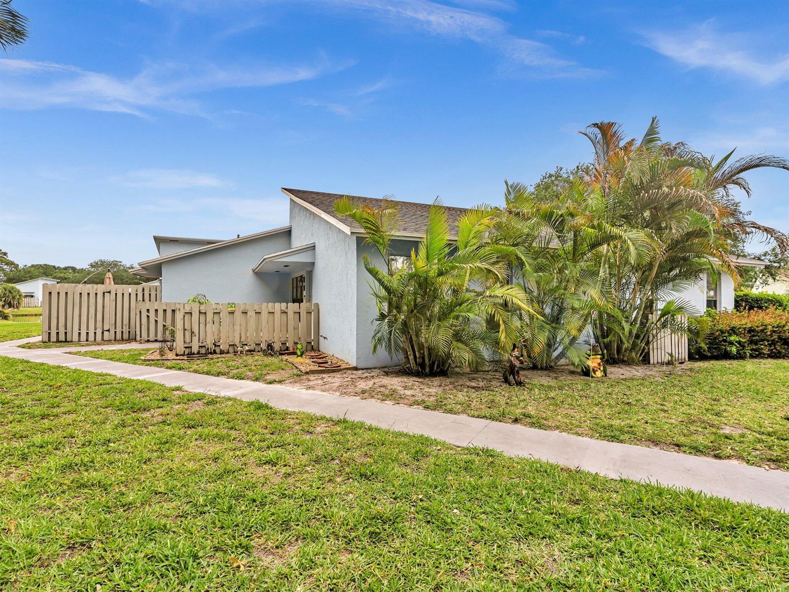 A light blue house with a sloped roof sits behind a wooden fence and palms — 431 Jupiter Lakes Boulevard # 2124d, Jupiter FL 33458, JUPITER, FL
