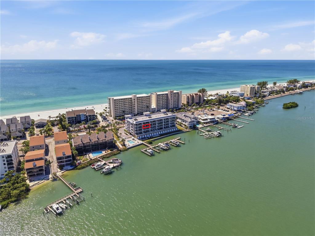 An aerial view shows a multi-story waterfront condominium complex with a boat dock — 20001 GULF BOULEVARD UNIT 405, INDIAN SHORES, FL